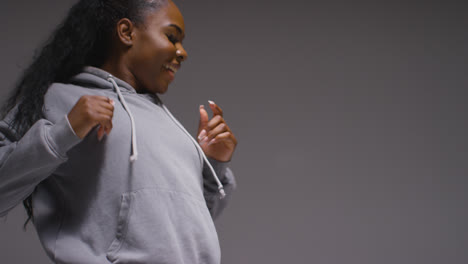 Studio-Portrait-Shot-Of-Young-Woman-Wearing-Hoodie-Dancing-With-Low-Key-Lighting-Against-Grey-Background-16
